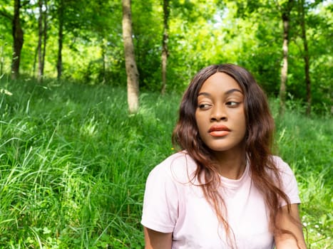 A woman is seated in the grass, her eyes closed in peaceful contemplation.