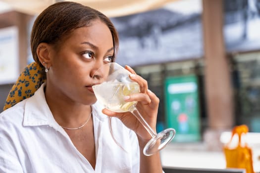 A sophisticated woman is seated at a desk, leisurely enjoying a glass of wine while gazing out at the bustling cityscape of Bilbao.