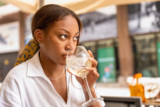 A sophisticated woman is seated at a desk, leisurely enjoying a glass of wine while gazing out at the bustling cityscape of Bilbao.