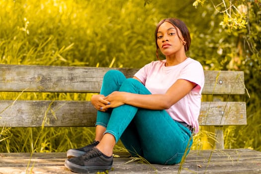 young black woman sitting on a bench in a park on a summer afternoon.