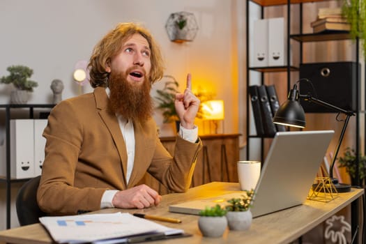 Young Caucasian entrepreneur prepares startup project for presentation finds idea. Confident redhead freelancer think typing browsing using laptop computer at home office desk. Remote distant working.