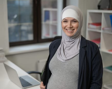 Pregnant Caucasian woman in hijab working in the office