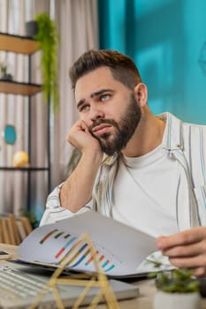 Frustrated upset businessman works at office desk laptop calculate looking at bills paperwork reports documents gets angry frustrated stress, bankruptcy financial problem. Freelancer at home. Vertical