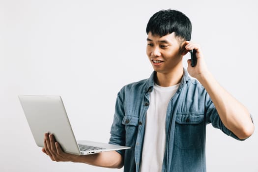 Portrait Asian smiling young man holding a laptop and talking on cell mobile phone studio shot isolated white background, Happy excited lifestyle businessman using computer and talking on smartphone