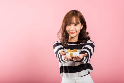 Portrait of happy beautiful Asian young woman smiling holding small gift box on hands, studio shot isolated on pink background, gift for you. Birthday, New year, Christmas, valentine day concept