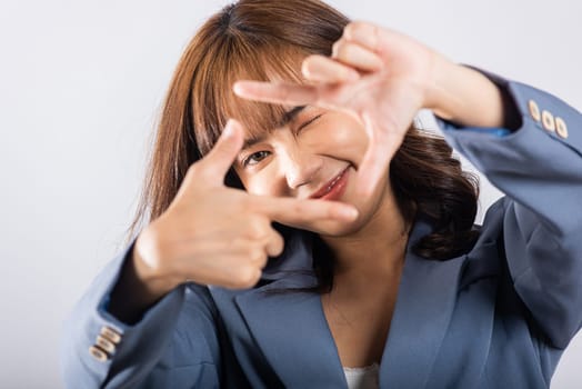 Portrait of a happy young business woman photographer framing with her finger in front of her face, capturing the concept of photography. Studio shot on white background, viewfinder sign