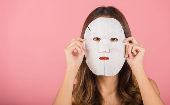 Portrait Asian young woman applying cosmetic paper sheet mask on her face studio shot isolated on pink background, beautiful female with natural makeup cosmetic mask, beauty skin care concept