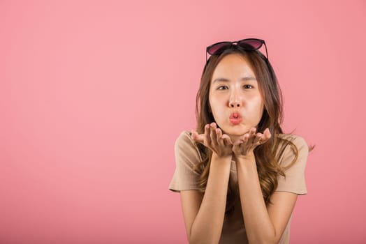 Asian happy portrait beautiful cute young woman teen standing blowing kiss air something on palm hands expresses her love looking to camera studio shot isolated on pink background with copy space