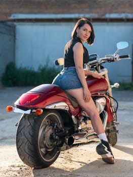 Brunette woman in shorts posing on a red motorcycle. Vertical photo