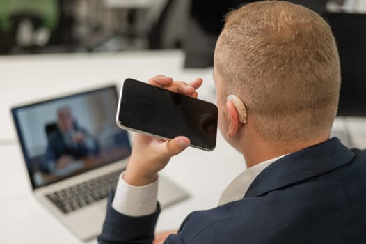 Caucasian man with a hearing aid talking on the phone on speakerphone