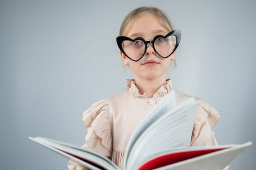 Portrait of a little girl in heart-shaped glasses reading a book