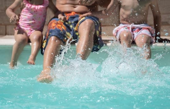 Unrecognizable family splashing water at the edge of the pool. Summer holidays concept.