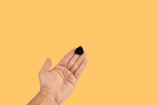 Black male hand holding a guitar pick isolated on yellow background. High quality photo