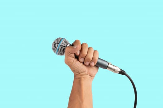 Black male hand holding a microphone isolated on light cyan background. High quality photo