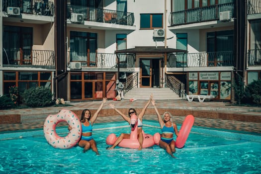 Three women are in a pool with inflatable toys, including a pink flamingo and a donut