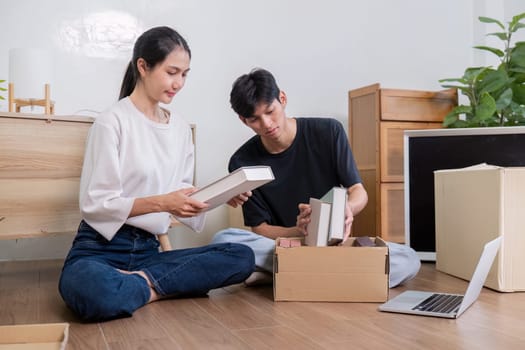 A young couple sits on the floor of their new home, unpacking boxes and organizing their belongings, symbolizing a fresh start and new beginnings.