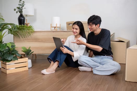 A young couple sitting on the floor of their new home, surrounded by moving boxes, using a laptop to plan their home decor.