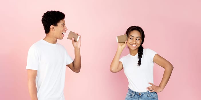 Communication and fun. Teen couple talking through tin can phone, pink background