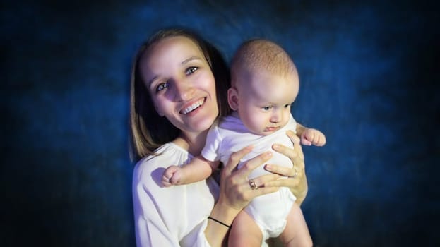 Mother holding her son in her arms. High quality photo. Portrait of Mother and Newborn Son on Blue Background