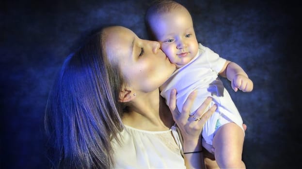 Mother kissing her child on the cheek. High quality photo. Mother and Child Portrait on Blue Background