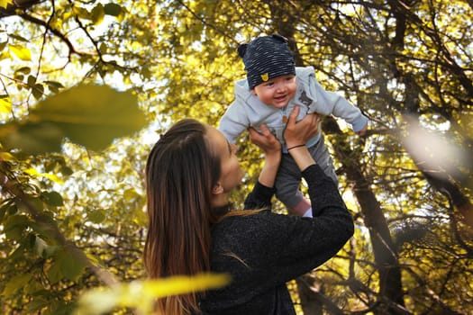 Mother holding her son in her arms. High quality photo. Portrait of mother and child in the rays of the sun among the trees