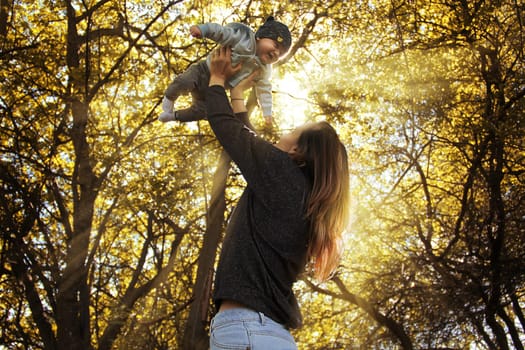 Mother holding her son in her arms. High quality photo. Portrait of mother and child in the rays of the sun among the trees