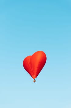 red heart shaped balloon soaring against a vibrant blue sky backdrop