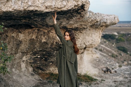 majestic woman in olive green coat standing on desert rock under blue sky