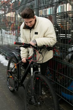 Young European man dressed in a winter jacket rides a bicycle.