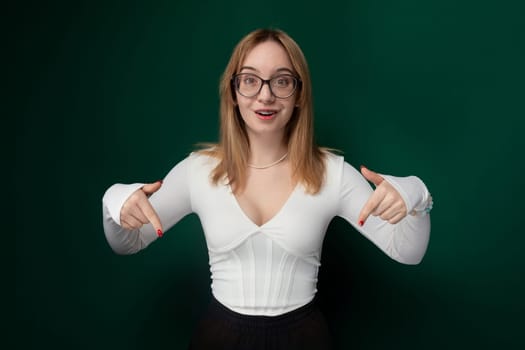 A woman with glasses is wearing a white shirt. She is standing upright, looking directly at the camera. Her hair is neatly styled, and she appears to be in a casual setting.