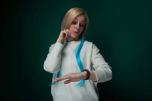 A woman wearing a white sweater is engaged in a phone conversation. She holds a cell phone to her ear while standing in an outdoor setting. The woman appears focused and attentive as she communicates through the phone.