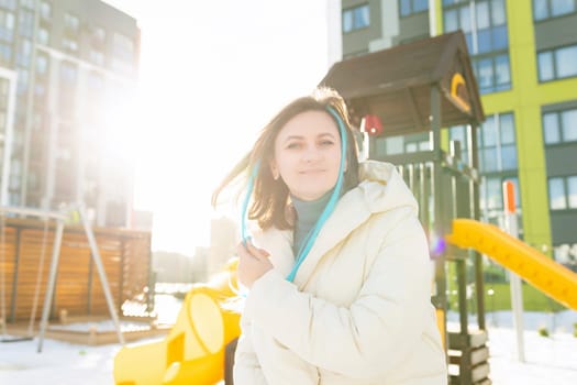 A woman is standing in front of a colorful playground with swings, slides, and climbing structures. The playground is empty, and the woman appears to be observing or waiting for someone.