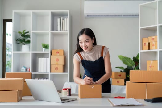 A young businesswoman prepares parcel boxes for delivery in a modern home office, showcasing the process of online ecommerce and product shipping.