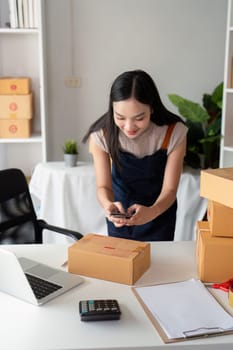 A young woman taking product photos and preparing parcel boxes for delivery in a modern ecommerce business setting.