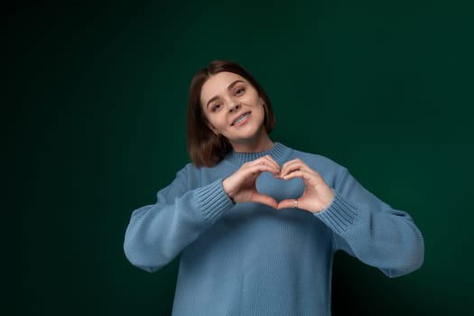 A woman standing with her hands positioned to form a heart shape in front of her chest.