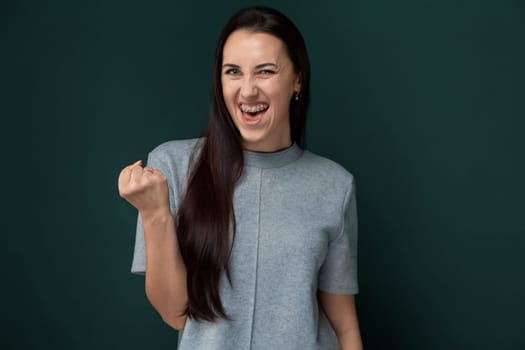 A woman with flowing long hair stands confidently in a gray shirt. Her hair cascades down her back as she strikes a pose.