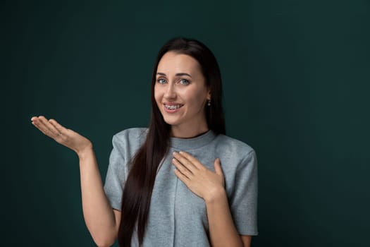 A woman with long hair is seen standing in front of a solid green wall. She appears to be looking straight ahead, with her hair flowing loosely around her. The background is a simple, unadorned green surface.