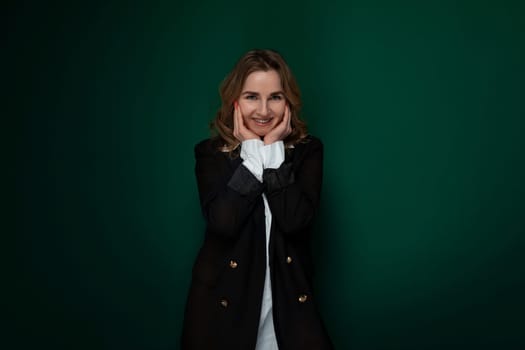 A woman is standing in a pose, with her hands covering her face as if framing it for a photograph. She appears confident and stylish as she strikes the pose for the camera. The background is simple, allowing her to be the main focus of the shot.