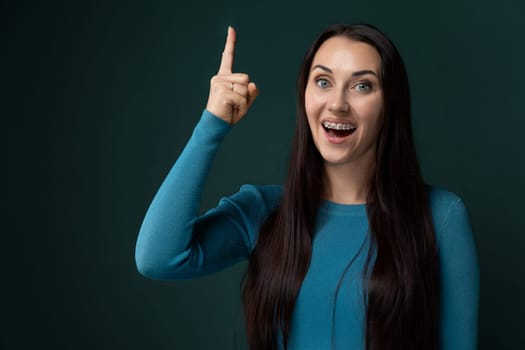 A woman with long black hair is pointing to the side in the image. She is dressed in casual attire and appears to be gesturing towards something off-camera. Her hair is flowing and shiny, drawing attention to her action.