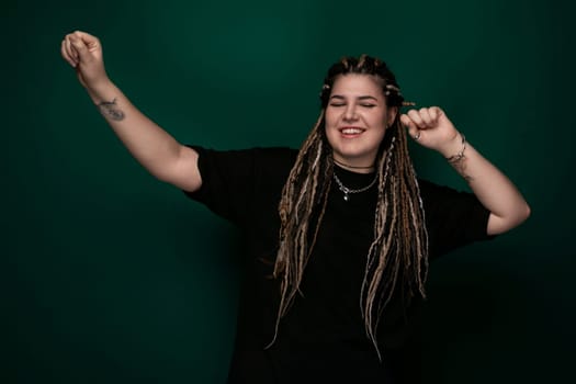 A woman with dreadlocks is standing in front of a vibrant green background. She is confidently looking at the camera. The green background contrasts with her dark hair, making her stand out.