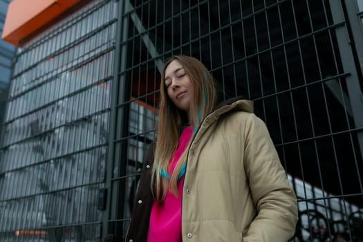 A woman in casual attire standing in front of a modern tall building, looking up towards the skyscraper. The building is made of glass and steel, reflecting the surrounding cityscape.