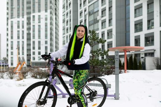 A woman is standing next to a bicycle in a snow-covered landscape. She is dressed in winter clothing and appears to be examining the bike.