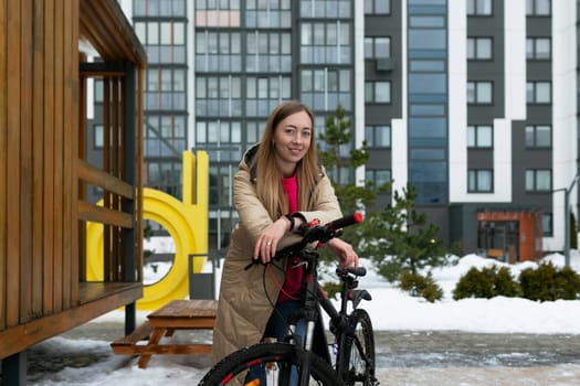 A woman is standing next to a bike in a snowy landscape. She is dressed warmly, and the bike is covered in snow. The scene conveys a winter atmosphere.