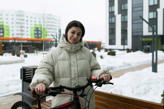 In the snowy landscape, a woman is dressed warmly, standing next to a bicycle. The snow-covered ground and the bicycle are prominently featured in the scene.
