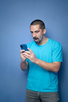 Happy young man amazed with mobile phone on blue background. High quality photo