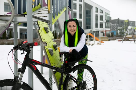 A woman in winter clothing standing next to a parked bike on a snowy path. The scene captures the contrast between the white snow and the dark colors of the bike and the womans outfit.