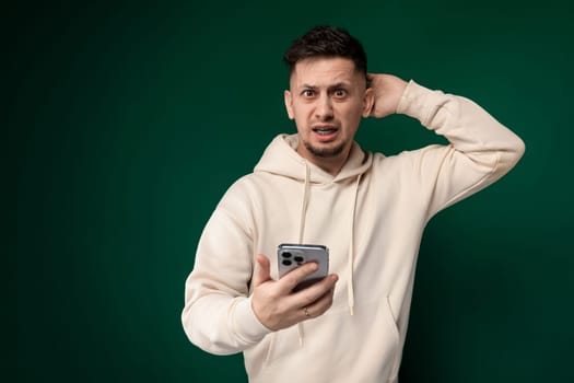A man wearing a hoodie is holding a cell phone in his hand. He appears focused on the screen as he interacts with the device.