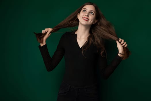A woman with long hair is standing in front of a vibrant green background. She appears confident and poised, her hair flowing freely around her. The simplicity of the background emphasizes her presence.