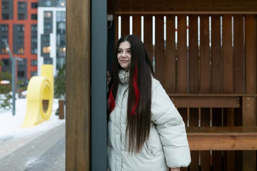 A woman with long hair is standing in front of a building. She appears calm and confident, looking straight ahead. The building features intricate architectural details and large windows. The scene conveys a sense of urban sophistication and modernity.