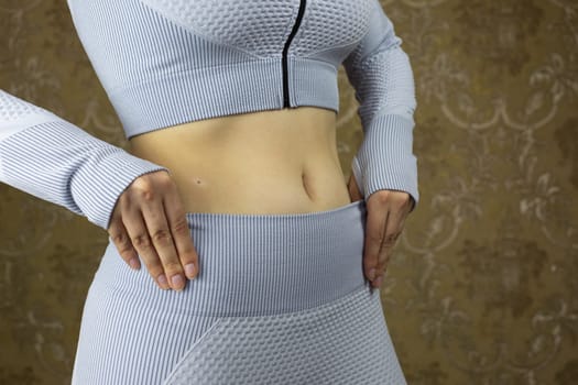 Female body in sports tight suit for training with open belly, girl pulls leggings on her waist before doing sports, concept of healthy life and sport